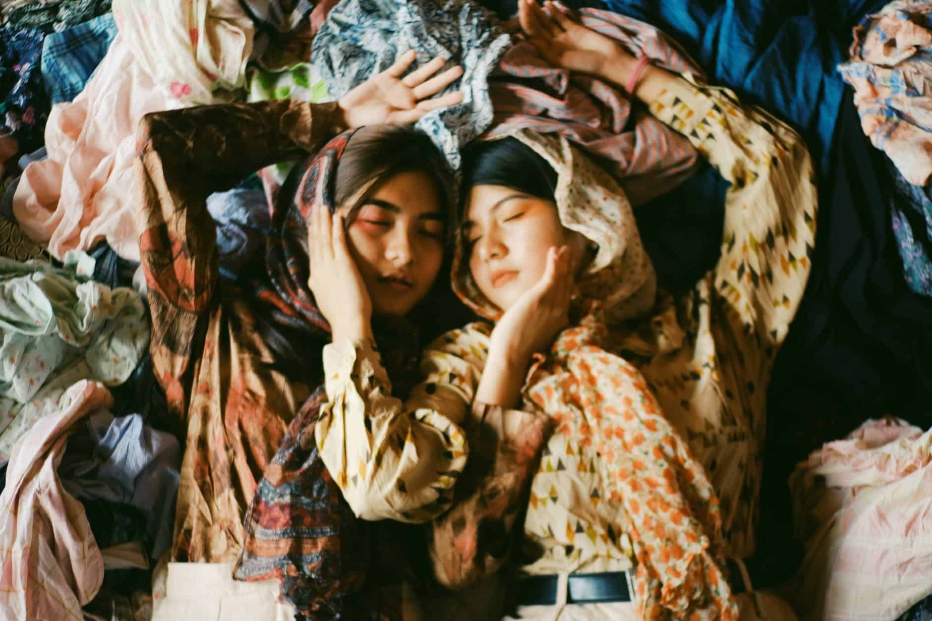 two women wearing earth toned printed tops and scarves lying on a pile of clothes