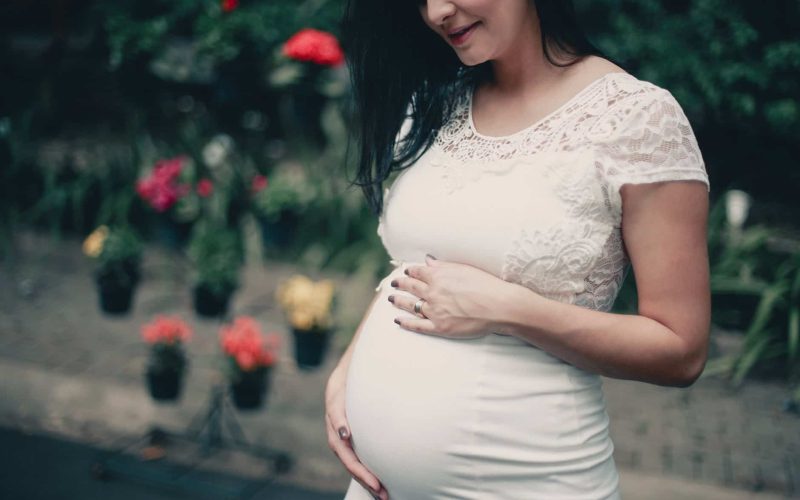 close up photo of pregnant woman in white dress holding her stomach