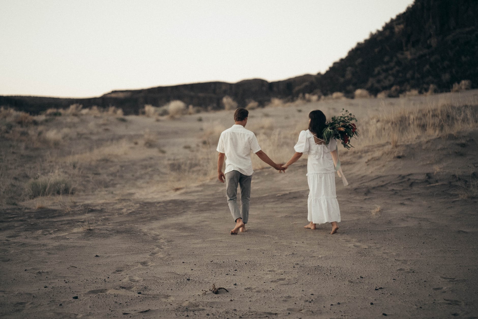 unrecognizable wedding barefoot couple walking on sandy terrain