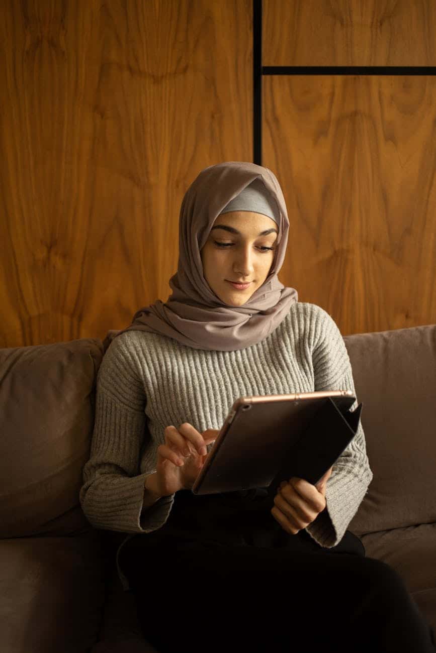 positive muslim woman using tablet on sofa