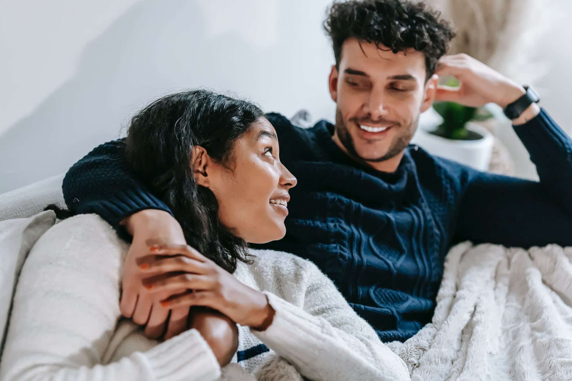 cheerful multiethnic couple resting on couch under blanket